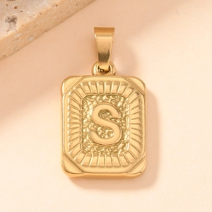 Macro detail of a golden rectangular pendant featuring a textured letter S design