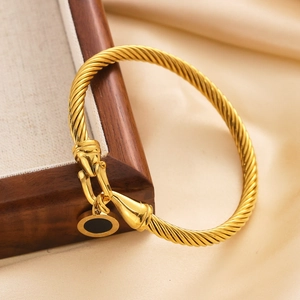 Detail of gold twisted cable bracelet with black Roman numeral charm on satin