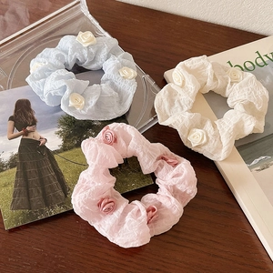Three camellia flower scrunchies in pastel blue, pink, and beige on a wooden table