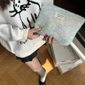 Detail of plush rainbow gradient cosmetic bag with woven brand label held by hand