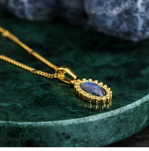Detail of 18K gold-plated oval blue abalone shell pendant on a green marble tray