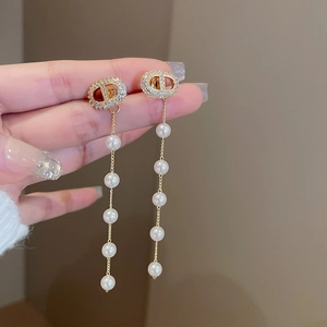 Detail view of gold tassel earrings with CD logo design and hanging white pearls