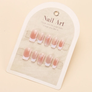 Pink press-on nails with white French tips and bow designs on a display card