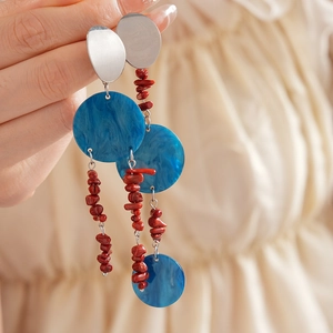 Detail of silver needle tassel earrings with blue resin and red beads on hand