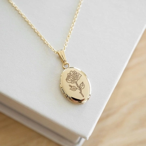 Oval gold locket necklace with rose engraving on white jewelry box background