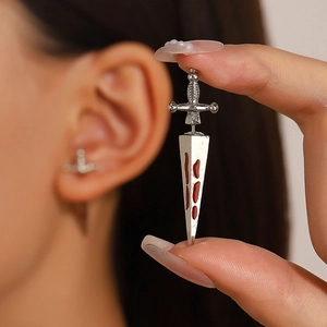Detailed close-up of a silver gothic dagger earring with red blood droplet accent
