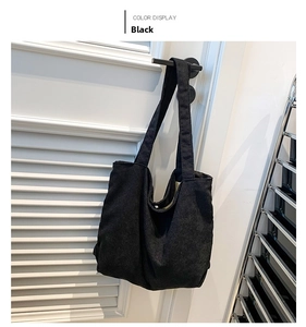 Detail of black corduroy tote bag showing vertical striped texture on white wooden door