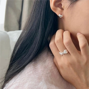 Close-up of 925 silver bow ring and heart earrings worn on model with soft lighting