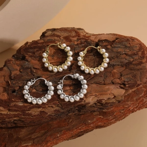 Close-up of pearl hoop earrings in gold and silver finish on a rustic wood bark surface