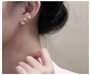 Close-up of three gold-plated sparkling stars stud earrings worn by a female model