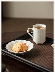 Detail of white ceramic teacup with floral embossing on a rustic dark wooden tray