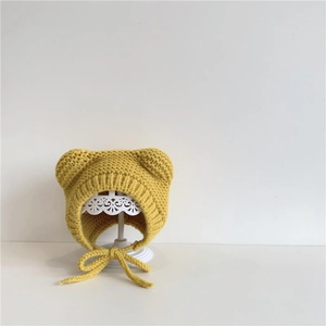 Detailed close-up of yellow knit baby bear hat with earflaps and soft braided ties