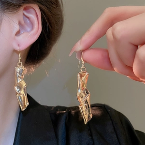 Close-up of golden irregular twisted geometric earrings with liquid metal texture on ears