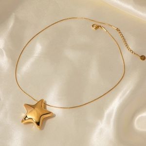 Detail view of a gold star pendant necklace on smooth beige silk fabric background