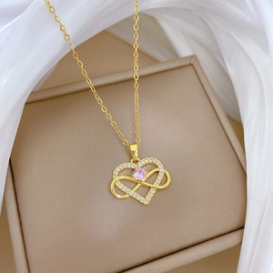 Close-up of golden heart and infinity pendant with pink gemstone on silk fabric