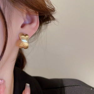 Detailed close-up of a matte gold twisted cross earring worn by a model