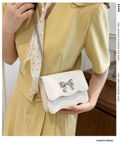 White chain shoulder bag featuring a silver bow detail shown with a yellow summer dress