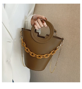 Detail of a brown bucket bag with circular handle and bold amber chain decoration