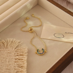 Close-up of golden horseshoe pendant bracelet with iridescent shell inlay and box chain