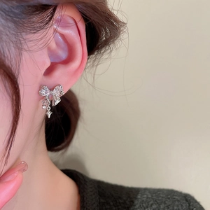 Close-up of sparkling bow earrings with star tassels on a model's ear, silver jewelry