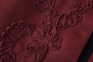 Macro shot of 3D floral embroidery on wine red textile fabric for elegant vest