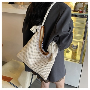 Detail of beige woven tote bag featuring white lace trim and fringe braided shoulder strap