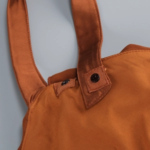 Detail of caramel satin dress showing shoulder strap attachment with black metal snap button