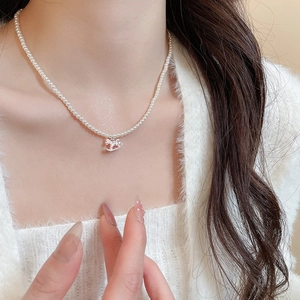 Detail of a pearl necklace with silver rocking horse pendant on white knit sweater