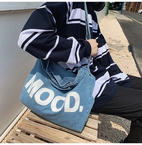 Detail of blue denim crossbody bag with large white MOOD. lettering in outdoor street setting