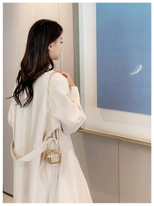 Detail of gold acrylic mini luggage bag with metal chain strap on white coat