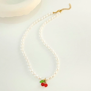 Close-up of white pearl necklace with red cherry pendant and adjustable gold chain