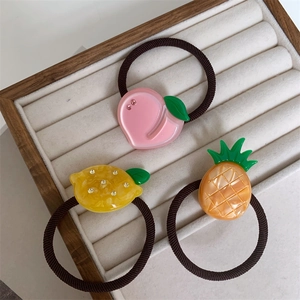 Three fruit-themed hair ties with peach, lemon, and pineapple charms in a jewelry box