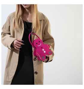 Detail of a bright magenta gingerbread-shaped felt handbag held by a model in a trench coat