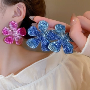 Close-up of oversized floral earrings with pink and blue crystals and silver needles