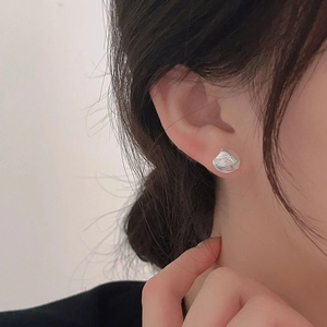 Close-up of a silver seashell stud earring worn by a model with a minimalist design
