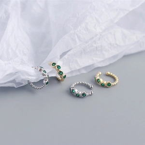 Detailed view of silver and gold ear cuffs with green stones on a textured background