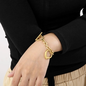 Detail of gold heart pendant necklace with OT toggle clasp on model's wrist