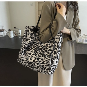 Quilted leopard print tote bag with black shoulder strap worn by a woman in a cafe