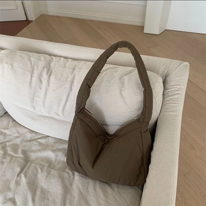 Detail of dark brown padded shoulder bag with zipper closure on a beige sofa