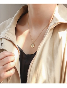 Close-up of gold star relief coin pendant necklace on model with soft natural lighting