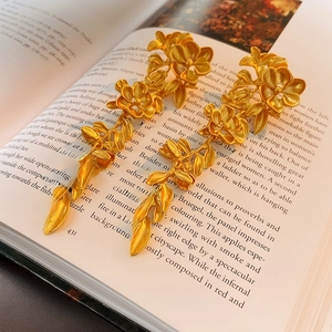 Close-up of vintage gold flower and leaf tassel earrings resting on an old book