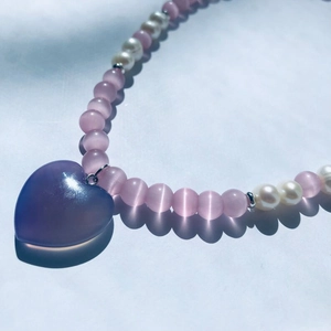 Close-up of heart-shaped purple pendant with cat-eye beads and elegant pearls
