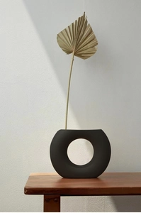 Detail einer mattschwarzen Keramikvase in Ringform mit getrocknetem Palmenblatt