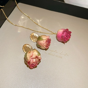 Close-up of pink dried rose jewelry set with resin petals and gold-plated details