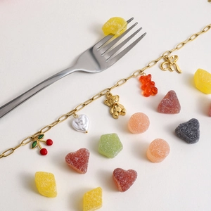 Detail of gold chain necklace with cherry, bear, and heart charms on a clean background