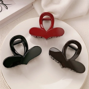 Three heart-shaped claw clips in dark red, black, and brown on a white gold-rimmed plate