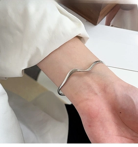 Primo piano di un bracciale rigido ondulato in argento al polso in uno stile moderno