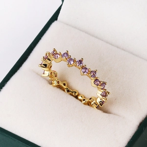 Golden wavy ring with purple cubic zirconia stones showcased in a dark green jewelry box