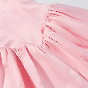 Detail shot of pink satin fabric showing elegant pleated texture and glossy stitching