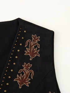 Détail d'un gilet en daim noir bohème avec broderie de feuilles et clous métalliques argentés